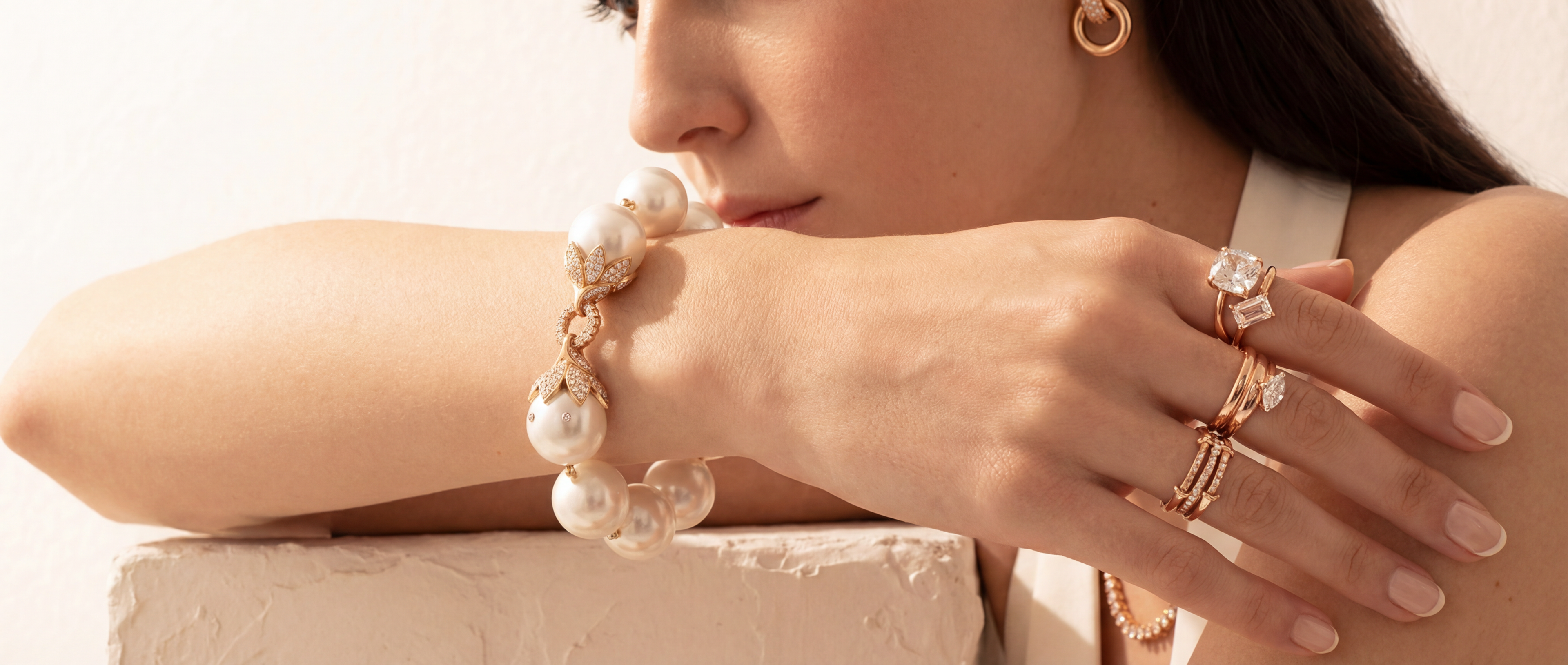 Close-up of a woman's hand wearing multiple rings and a pearl bracelet against a neutral background